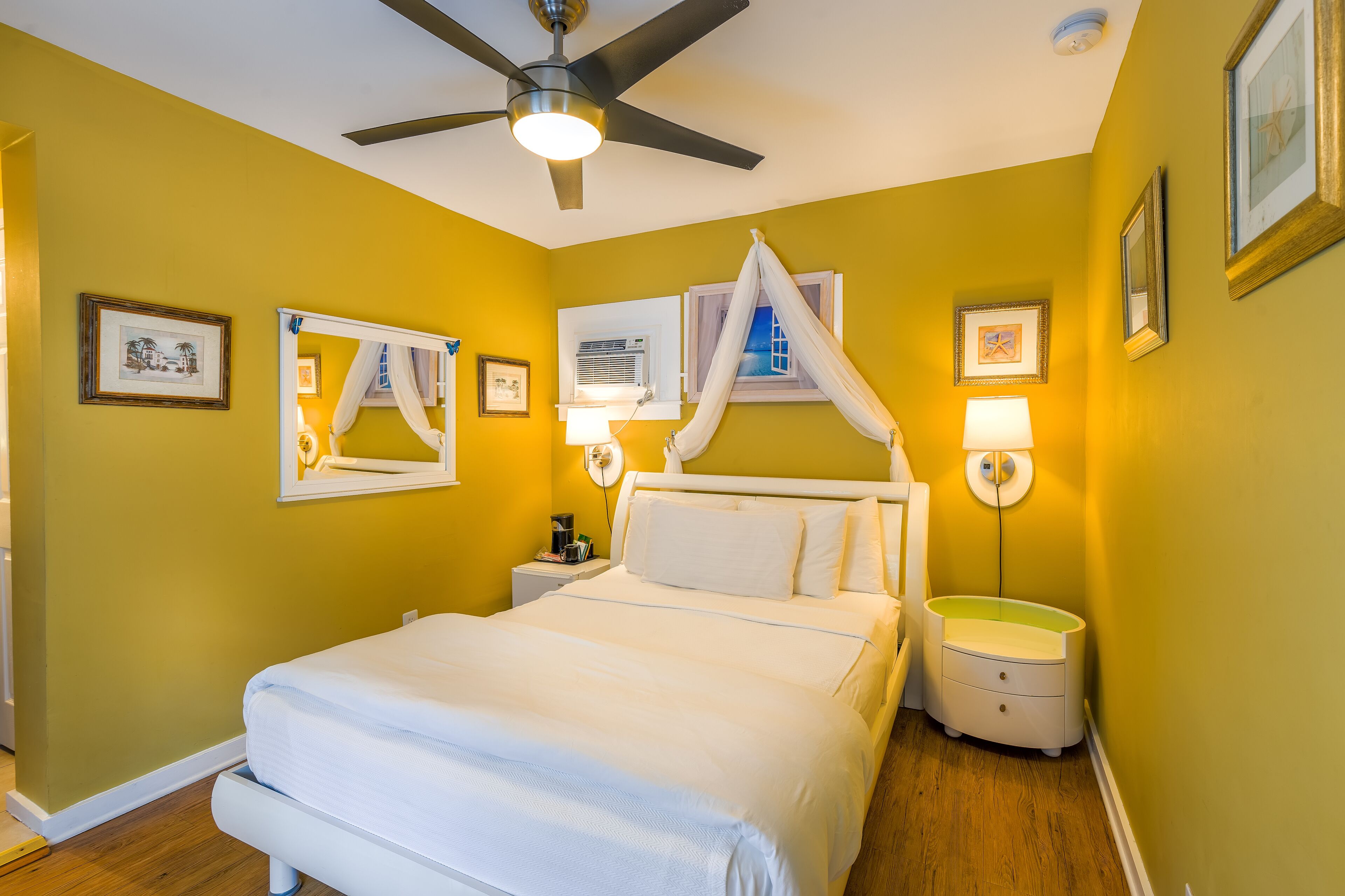 A bedroom with a bed, a ceiling fan, bedside lamps, and framed pictures on the walls.