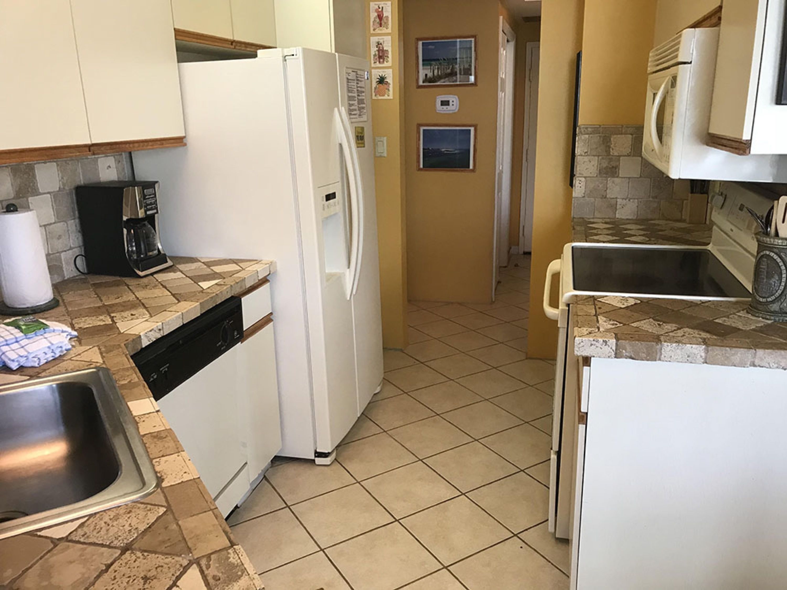 A compact kitchen with a white refrigerator, a coffee maker, and a dishwasher.
