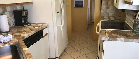 A compact kitchen with a white refrigerator, a coffee maker, and a dishwasher.