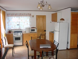 A compact kitchen with a stove, microwave, refrigerator, and a dining table with chairs.