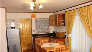 A compact kitchen with wooden cabinets, a refrigerator, and a dining table with chairs. - Turismo Vinapu (Hanga Roa)