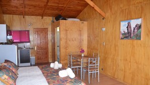 A wooden cabin with a bed, a small kitchenette, a dining area, and a painting on the wall. - Turismo Vinapu (Hanga Roa)