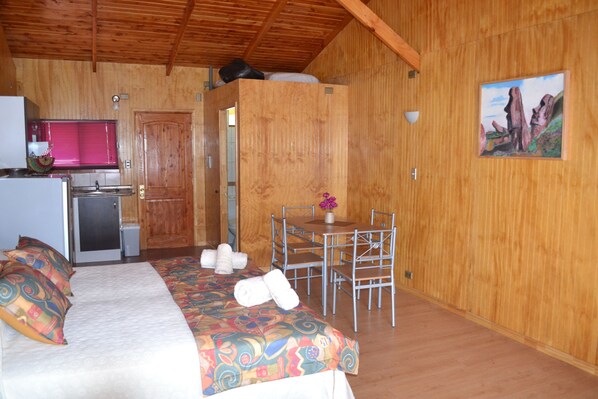 A wooden cabin with a bed, a small kitchenette, a dining area, and a painting on the wall.