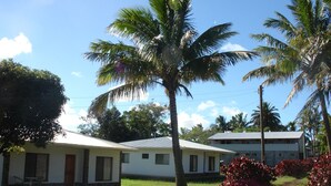A two-story building with a flat roof, surrounded by palm trees and a well-maintained lawn. - Turismo Vinapu (Hanga Roa)