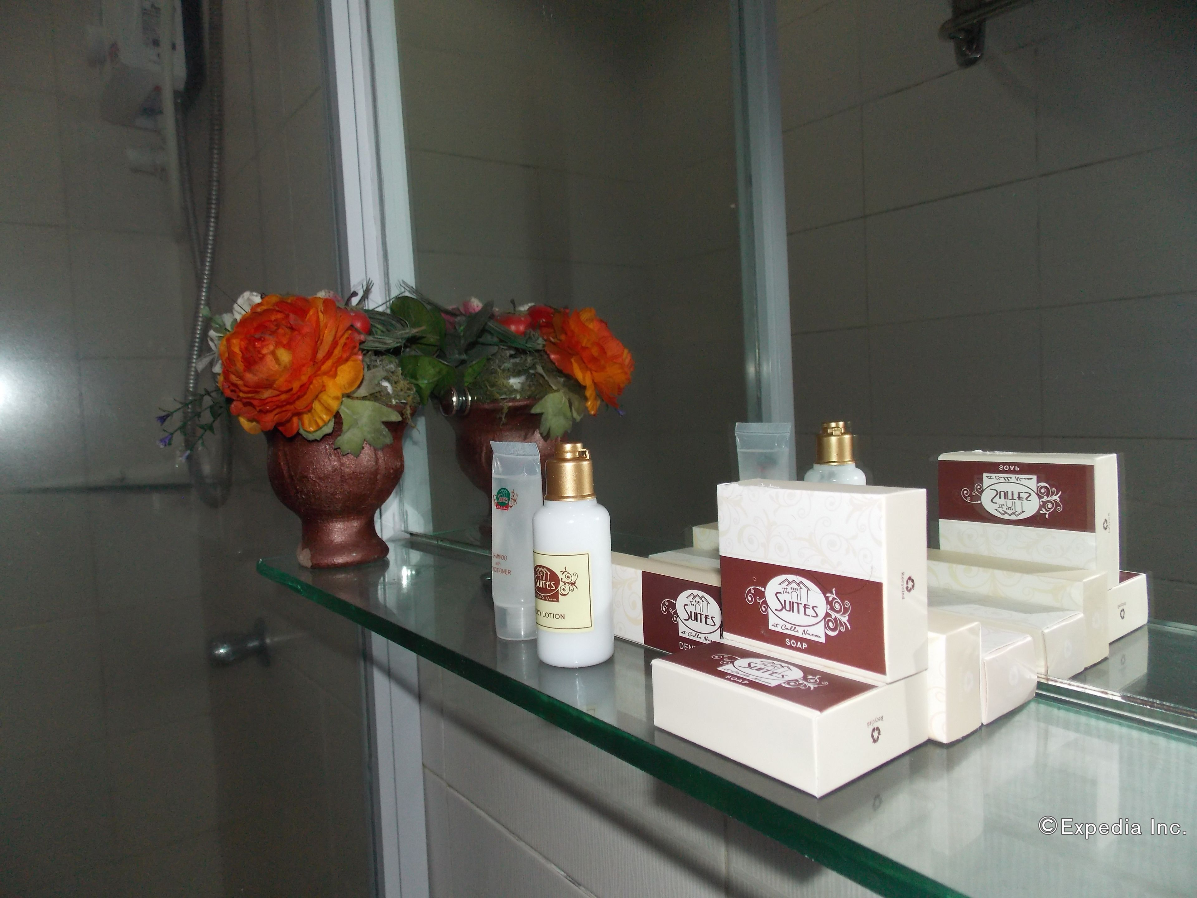 A bathroom with a glass shelf displaying toiletries, a mirror, and decorative flowers.