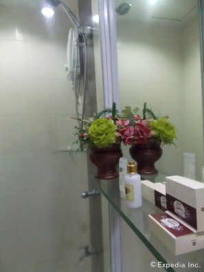 A bathroom with a glass shower enclosure, a mirror, and toiletries on a shelf.