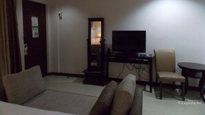 A living room with a sofa, a television on a stand, a chair, and a small table. - The Suites at Calle Nueva (Bacolod)