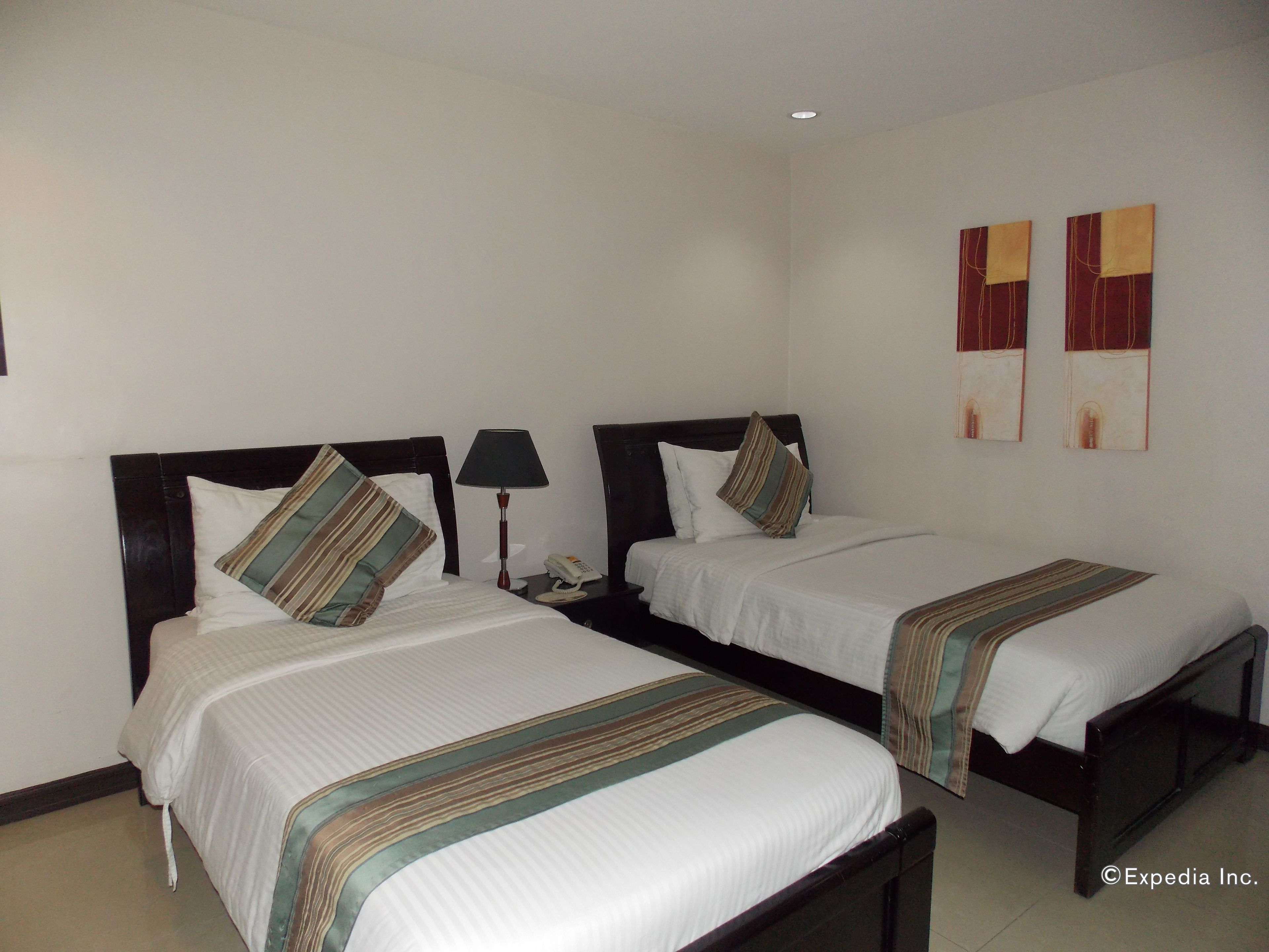 A hotel room with two single beds, each with a pillow and a bedside table with a lamp.