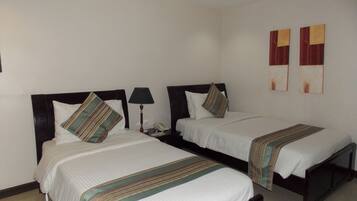 A hotel room with two single beds, each with a pillow and a bedside table with a lamp.