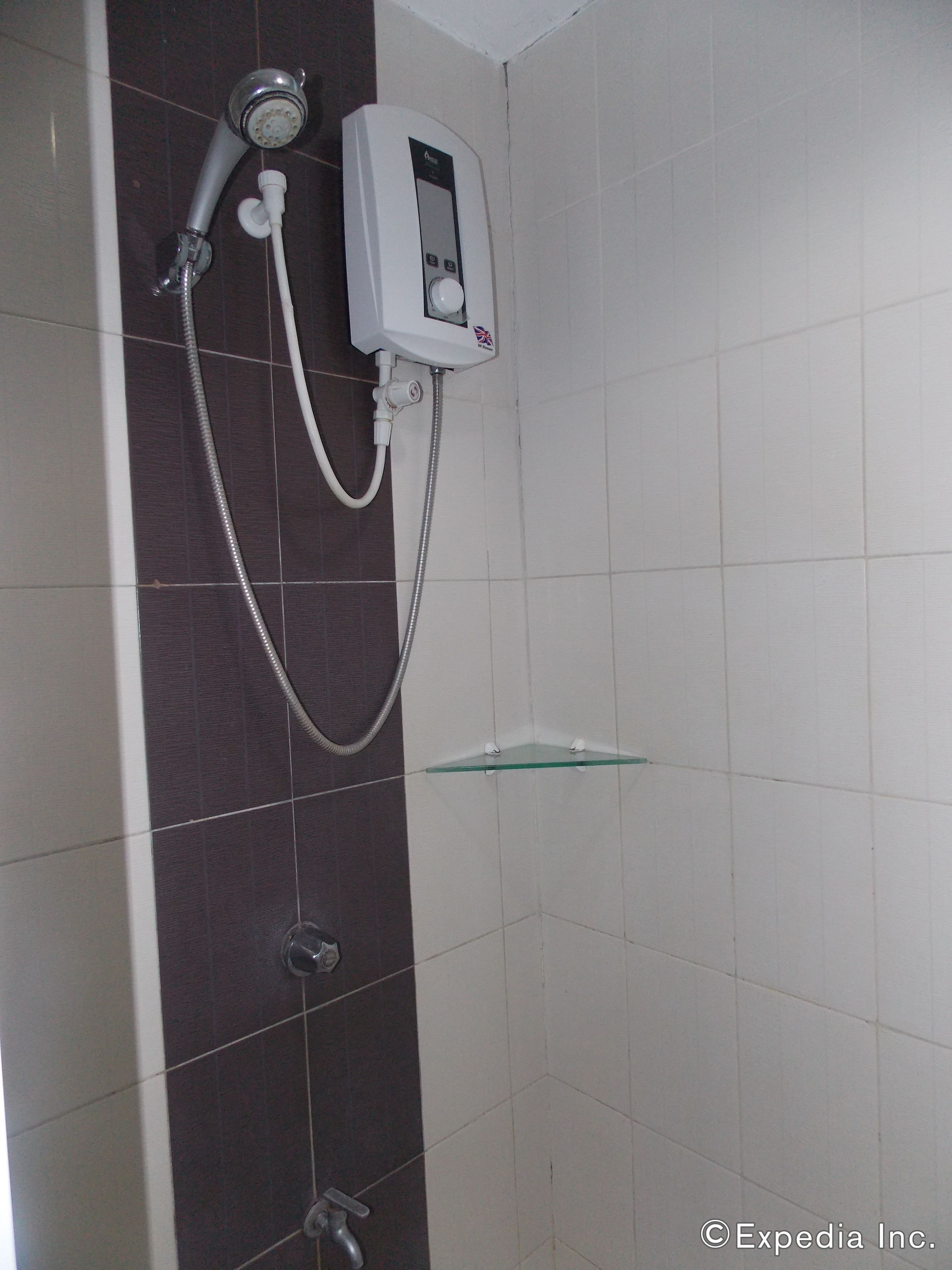 A shower with a handheld showerhead, a control panel, and a glass shelf.