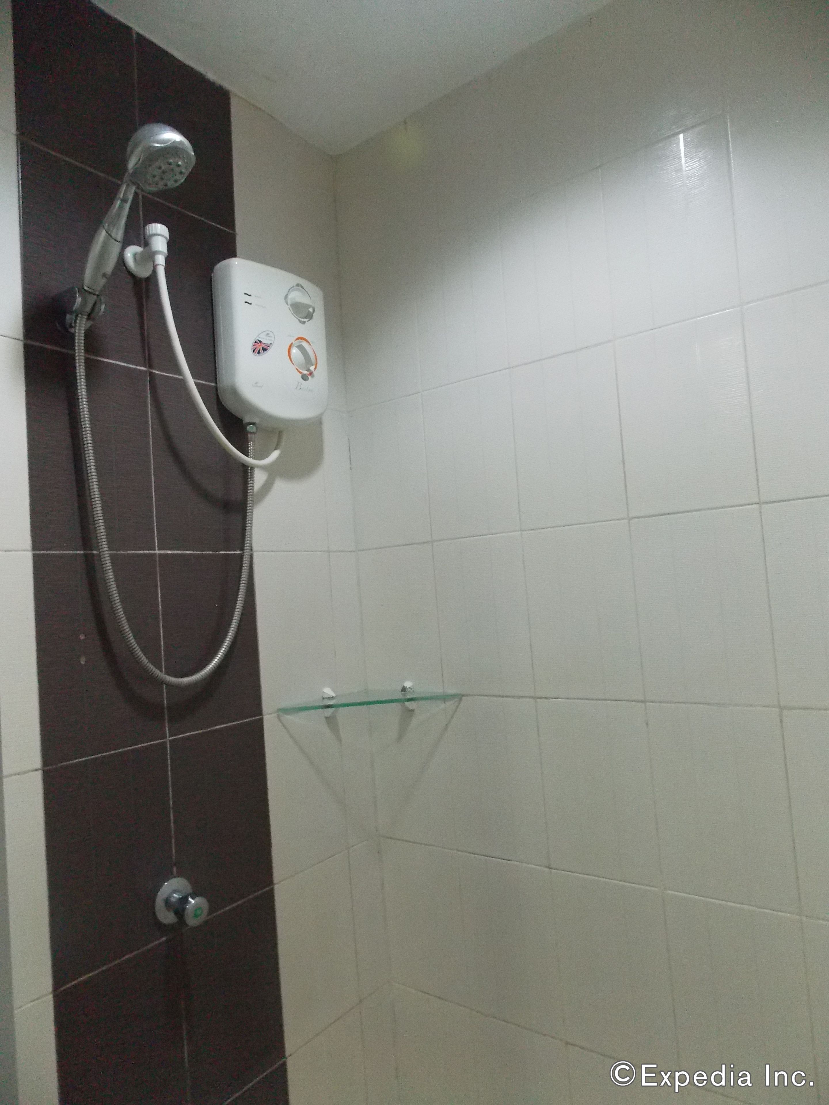 A bathroom with a shower, a glass shelf, and a white tiled wall.