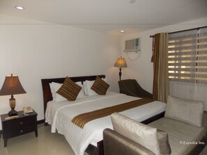 Een hotelkamer met een bed, nachtkastjes, een lamp, een stoel, een raam met zonwering en een airconditioning.