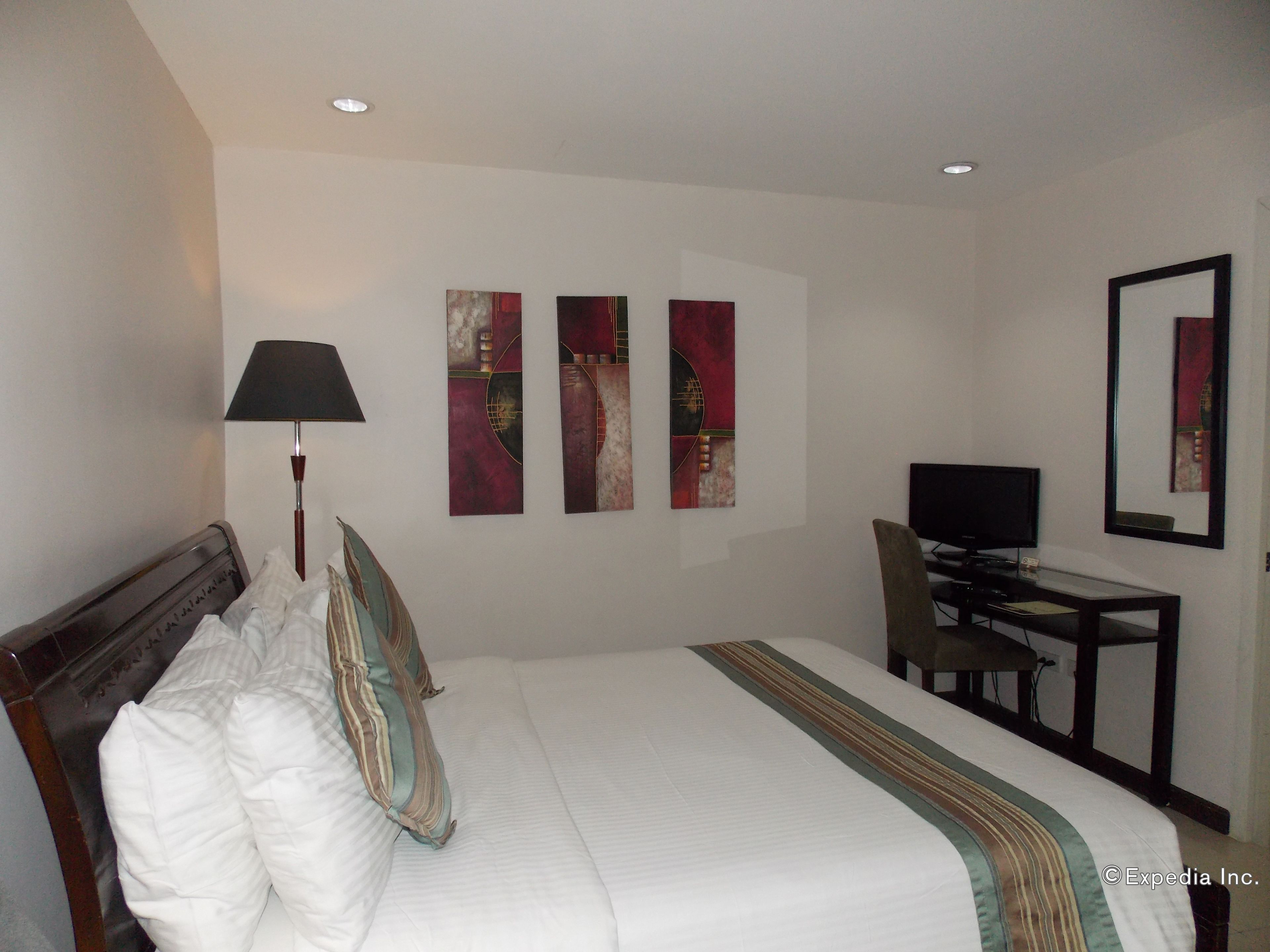 A hotel room with a bed, a desk, a television, and three abstract paintings on the wall.