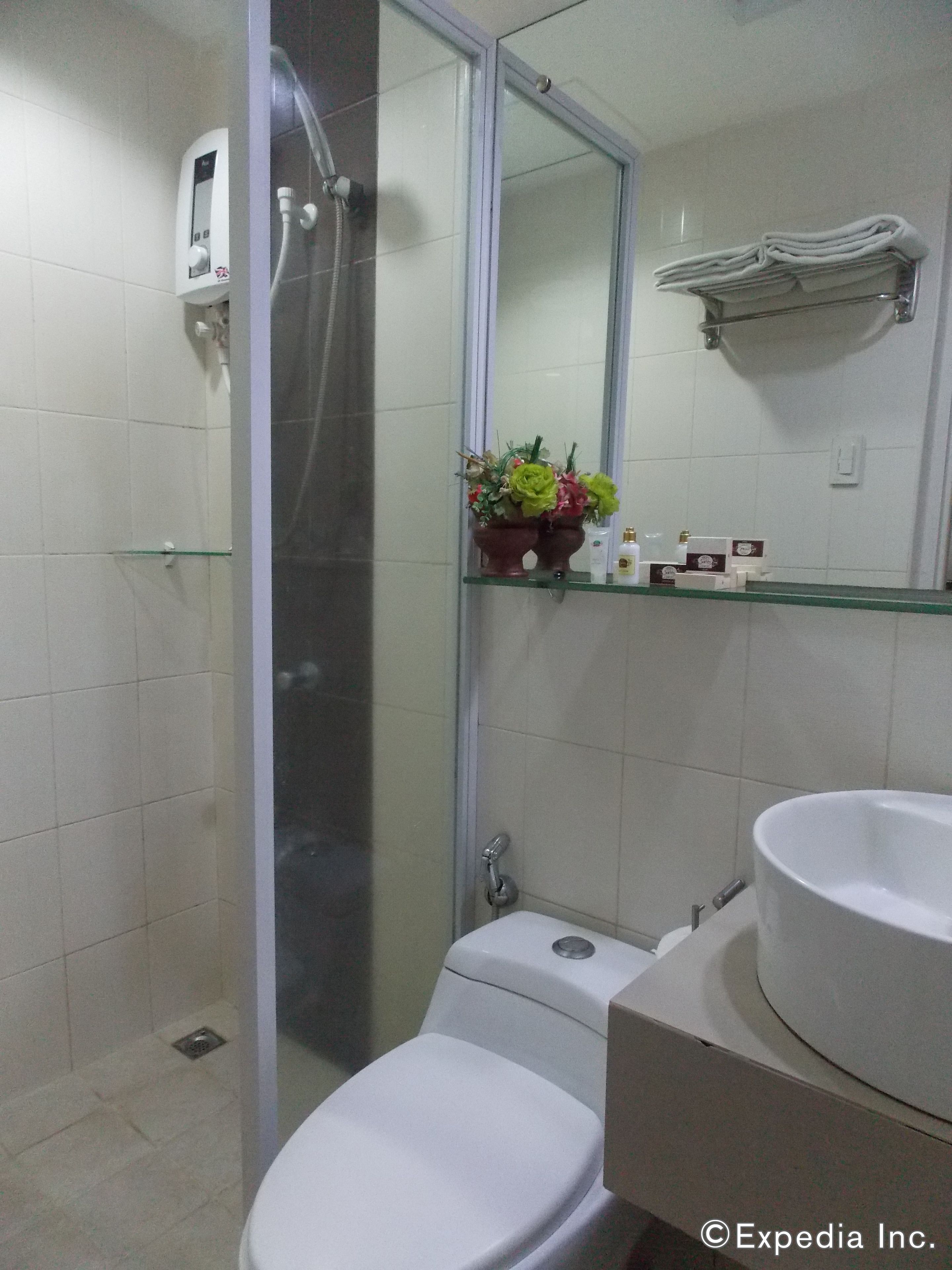 A bathroom with a toilet, a sink, a glass shower enclosure, a mirror, and a shelf with toiletries.