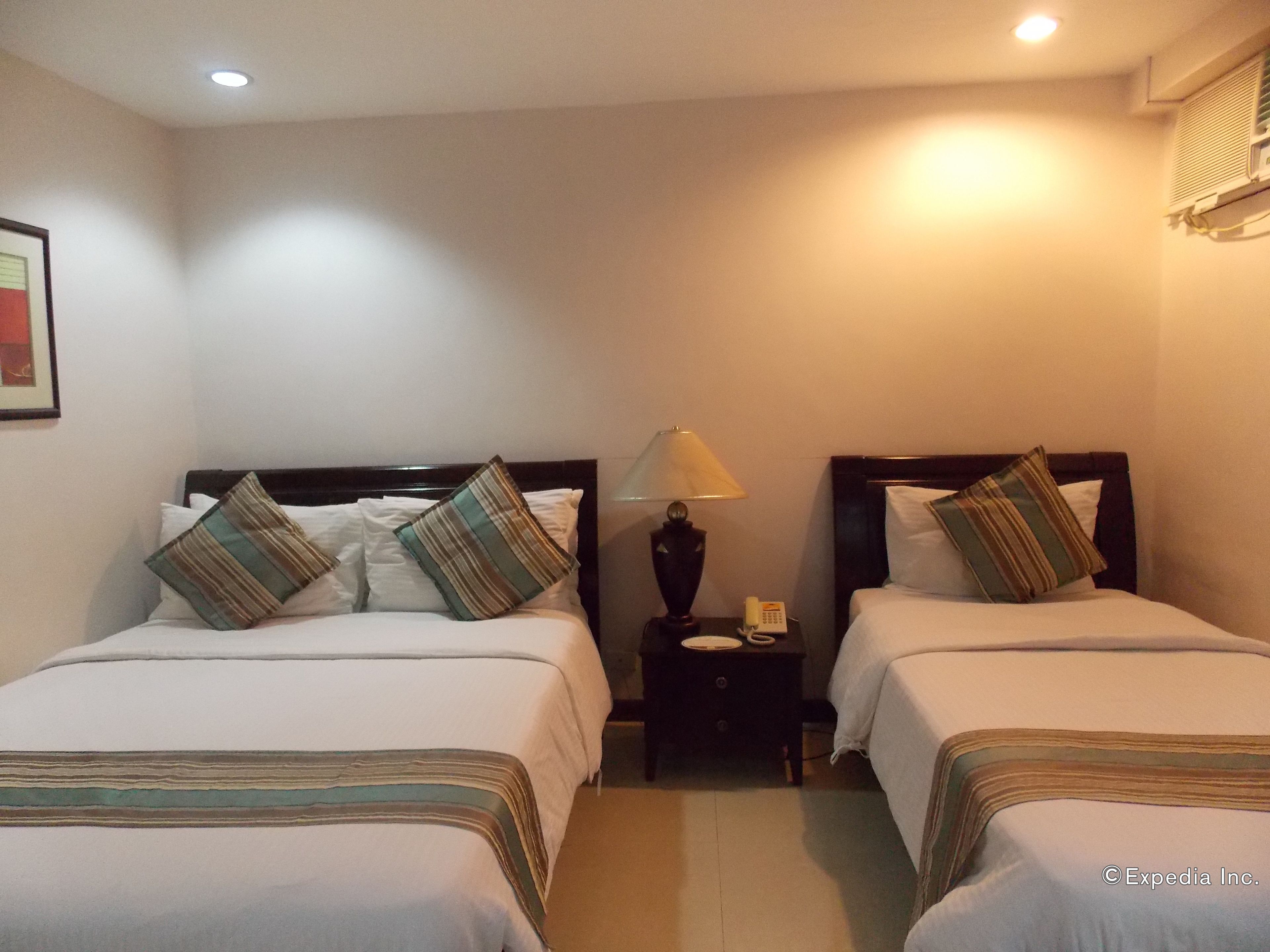 Habitación de hotel con dos camas, cada una con ropa de cama y almohadas a rayas, una mesita de noche con lámpara y teléfono.