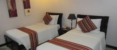 A hotel room with two single beds, each with a striped bedspread and pillows. There is a nightstand with a lamp and a phone between the beds.