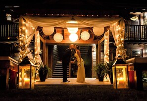 Una pareja besándose bajo un toldo con luces colgantes y faroles, con una escalera y paredes de madera al fondo.