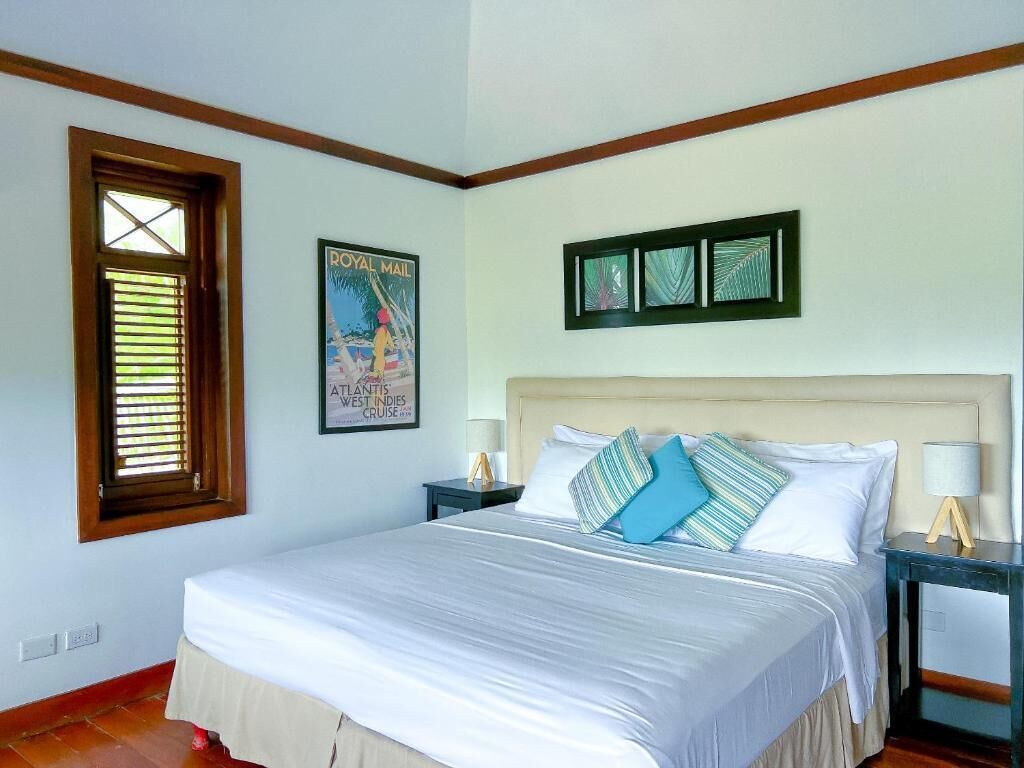 A bedroom with a large bed, two bedside tables, a window with blinds, and a framed picture on the wall.