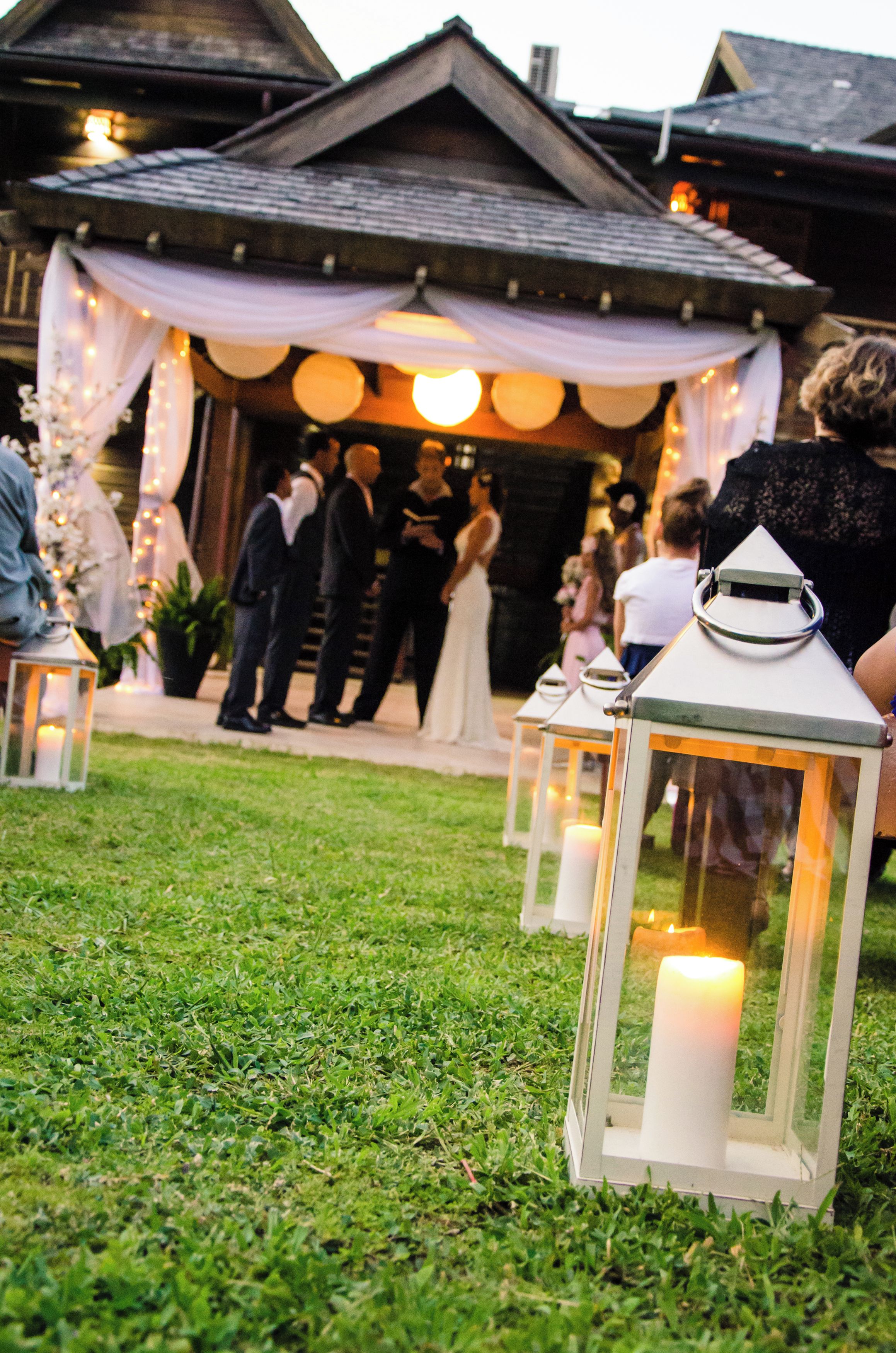 Una ceremonia de boda con invitados sentados sobre la hierba, un dosel blanco y velas encendidas.