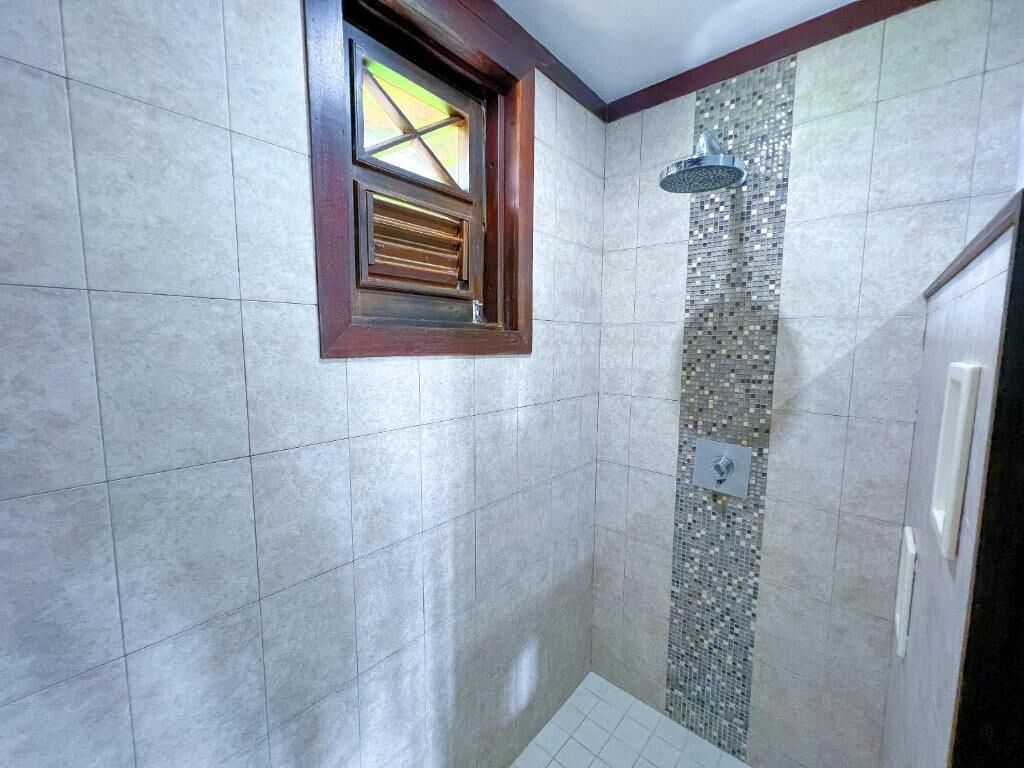 A bathroom with tiled walls, a shower with a rain showerhead, and a window with wooden blinds.