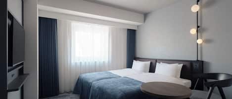A hotel room with a bed, a desk, a chair, a TV, and a window with curtains.