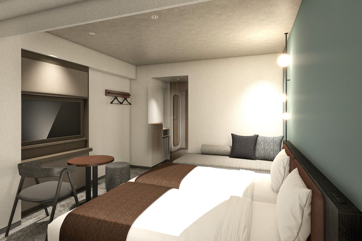 A hotel room with a bed, a TV, a small table, a chair, and a sofa.