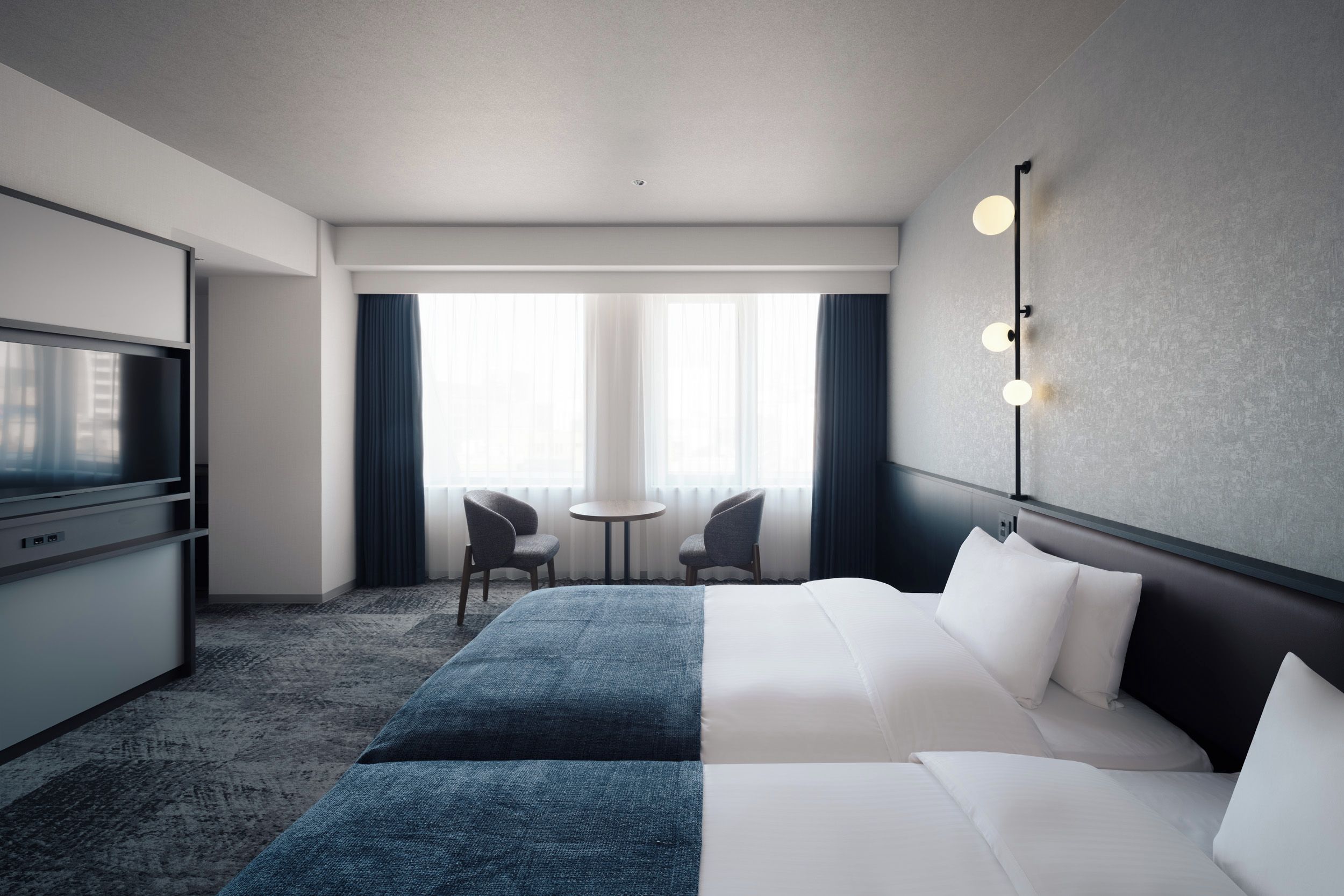 A hotel room with a bed, a desk, a television, two chairs, and a window with curtains.