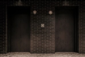 A modern elevator with a black brick wall design, a simple control panel, and two circular light fixtures. - Nest hotel alt. Sapporo odori (Sapporo)