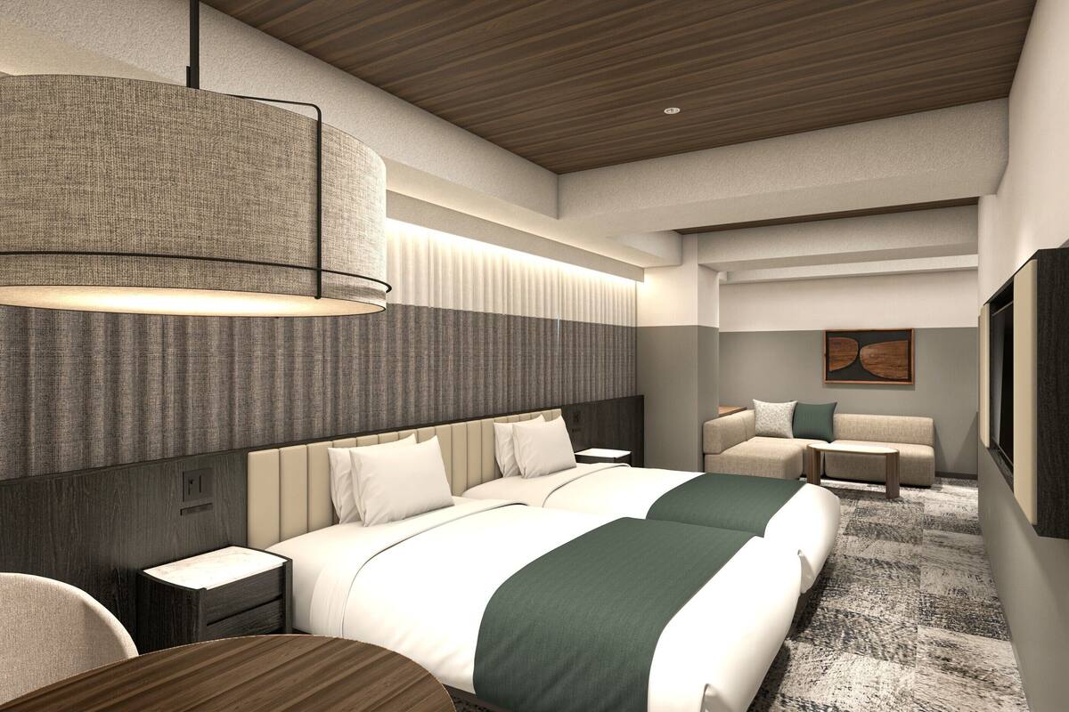 A modern hotel room with a large bed, a bedside table, a seating area with a sofa and armchair, and a large wall-mounted artwork.