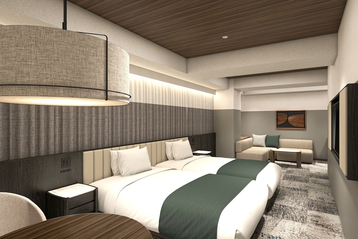 A modern hotel room with a large bed, a bedside table, a seating area with a sofa and armchair, and a large wall-mounted artwork.