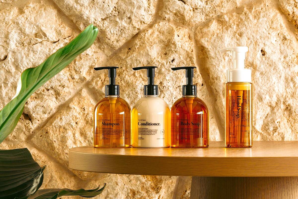A wooden shelf with four bottles of personal care products against a textured stone wall.