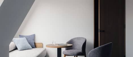 A modern loft bedroom with a sloped ceiling, a sofa, two armchairs, a small round table, and a door.
