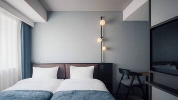 A hotel room with a bed, two pillows, a desk with a chair, a TV, and a wall-mounted light fixture.