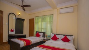 A hotel room with two beds, a ceiling fan, a mirror, and a window with green curtains. - Kathmandu Friendly Home (Kathmandu)