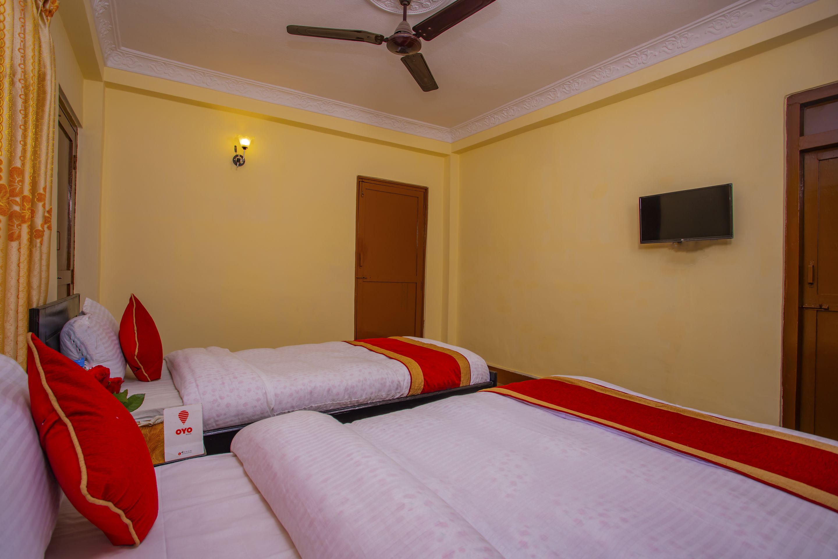 A hotel room with two beds, a ceiling fan, a television, and a door.
