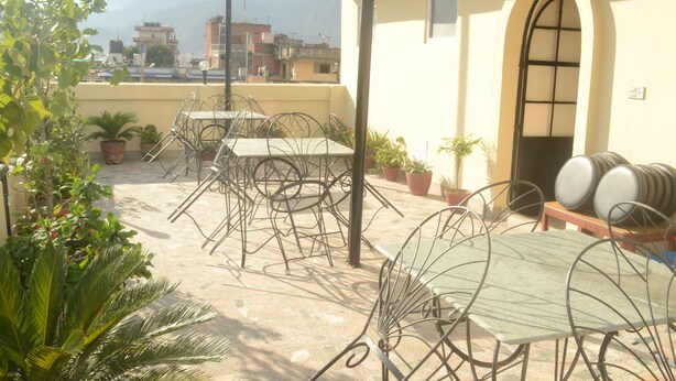 A rooftop patio with metal tables and chairs, potted plants, and a view of the cityscape and mountains in the background. - Kathmandu Friendly Home (Kathmandu)