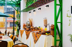 Un restaurante con mesas cubiertas por manteles naranja y blanco, una estructura metálica verde, y diversos productos alimenticios y bebidas a la vista.