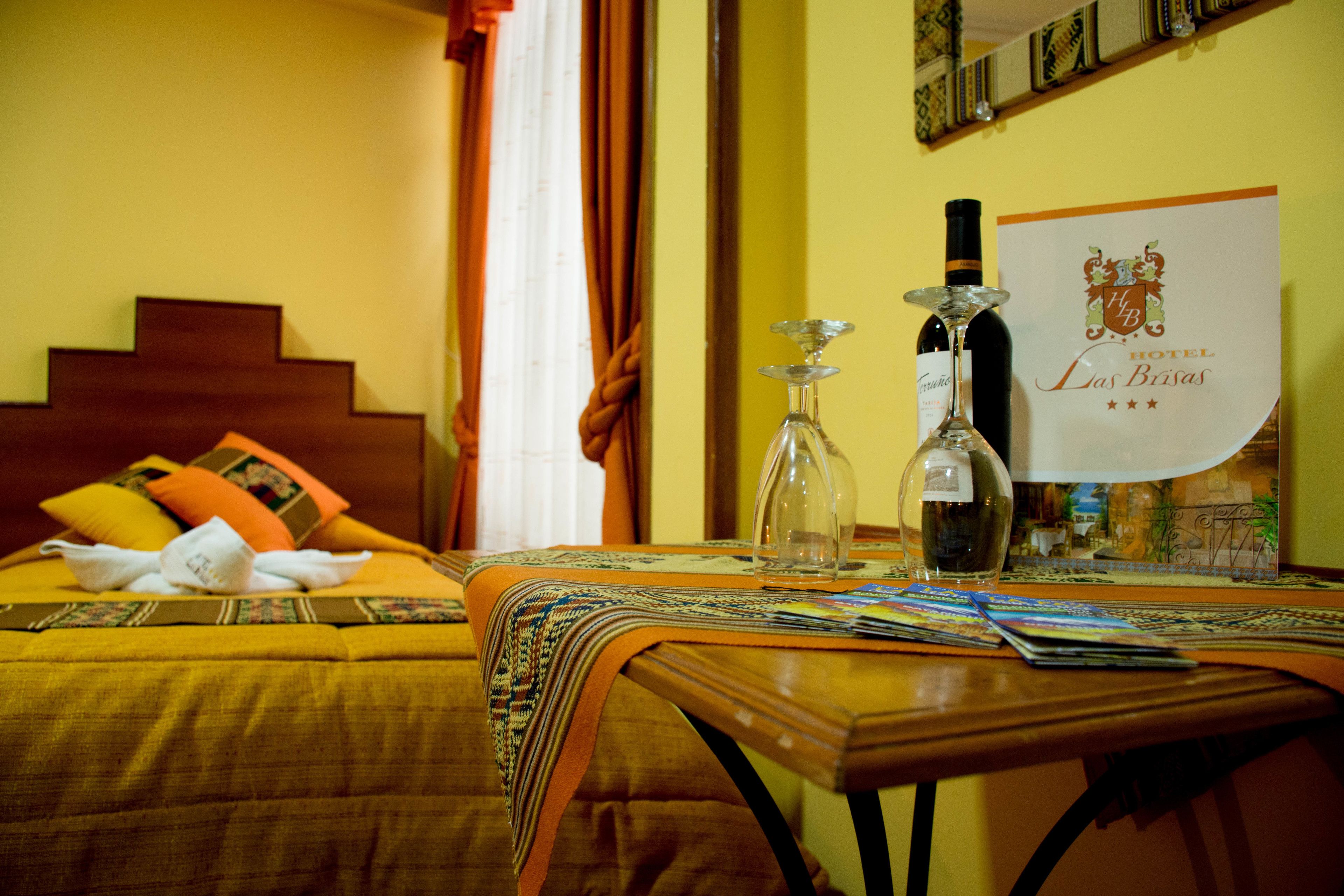 A hotel room with a bed, a table with a wine bottle and glass, and a sign with the hotel's name.