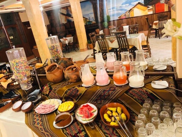 A buffet table with various food items and drinks, including fruits, pastries, and beverages in pitchers.
