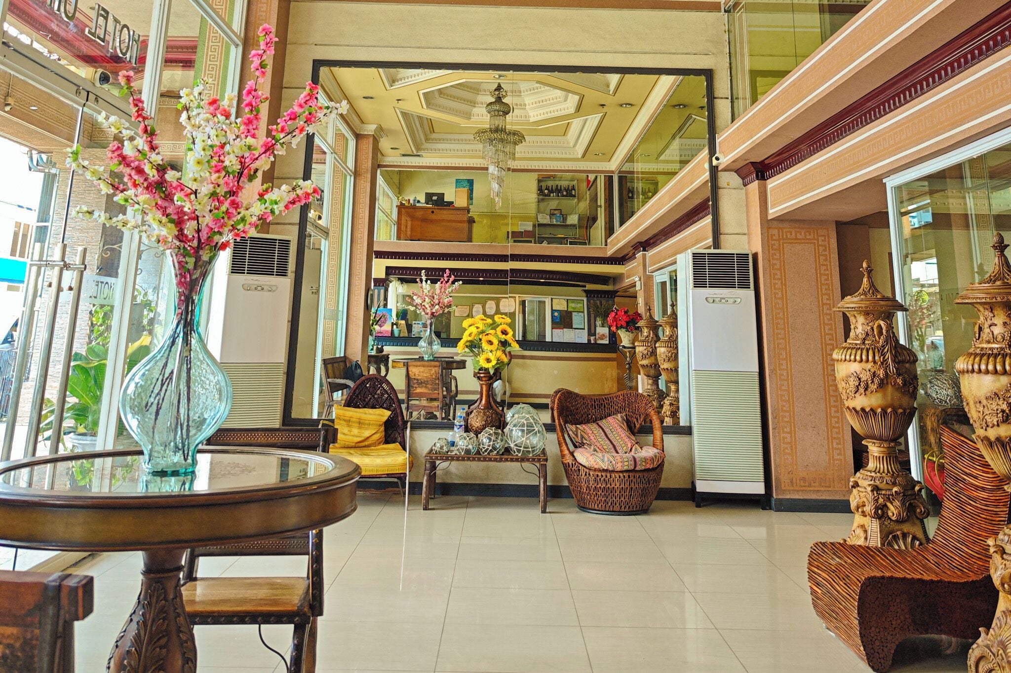 A hotel lobby with a glass coffee table, wicker chairs, a vase with flowers, and ornate vases.
