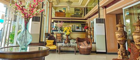 A hotel lobby with a glass coffee table, wicker chairs, a vase with flowers, and ornate vases.