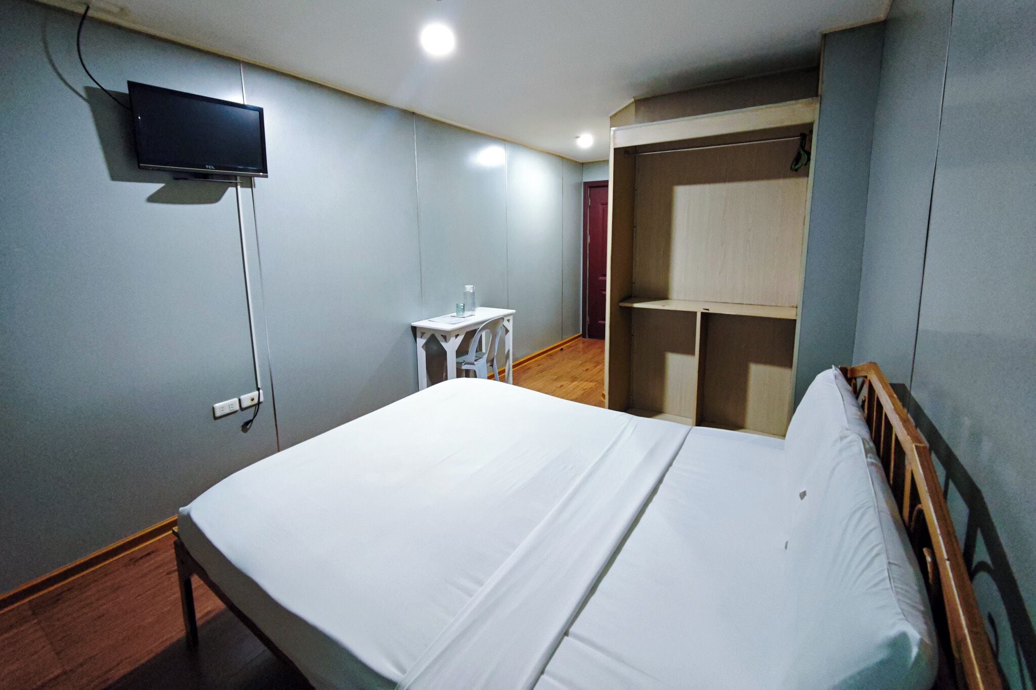 A bedroom with a bed, a TV mounted on the wall, a small table with a bottle, and a closet.