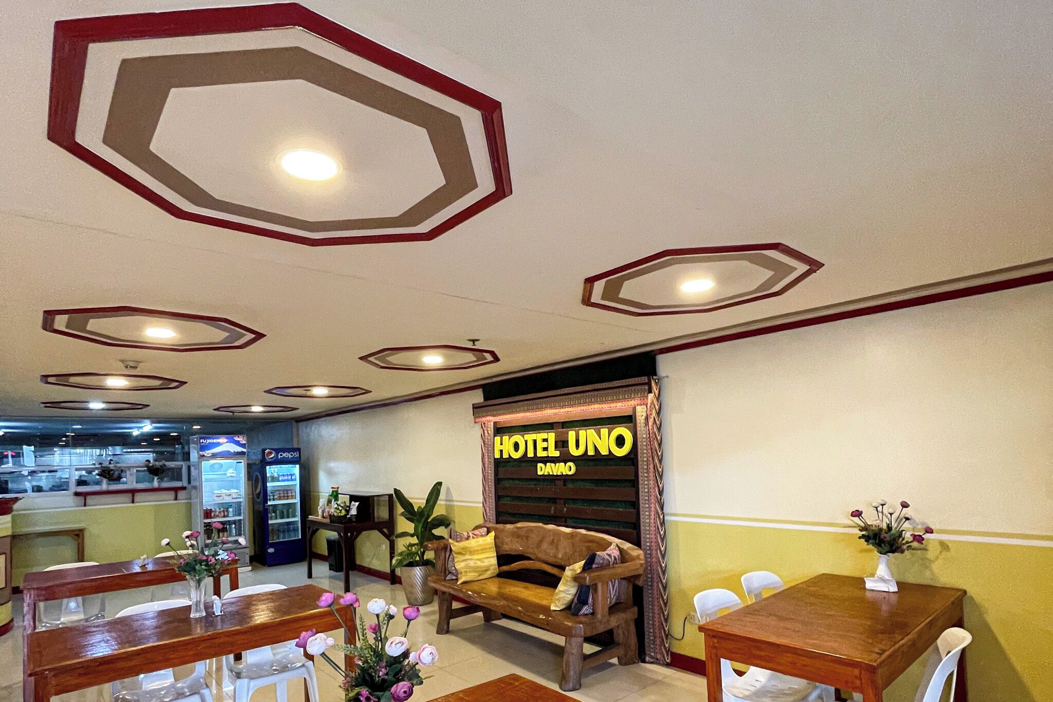 A hotel lobby with a wooden bench, a reception desk, and a sign reading 'HOTEL UNO DAVAO'.