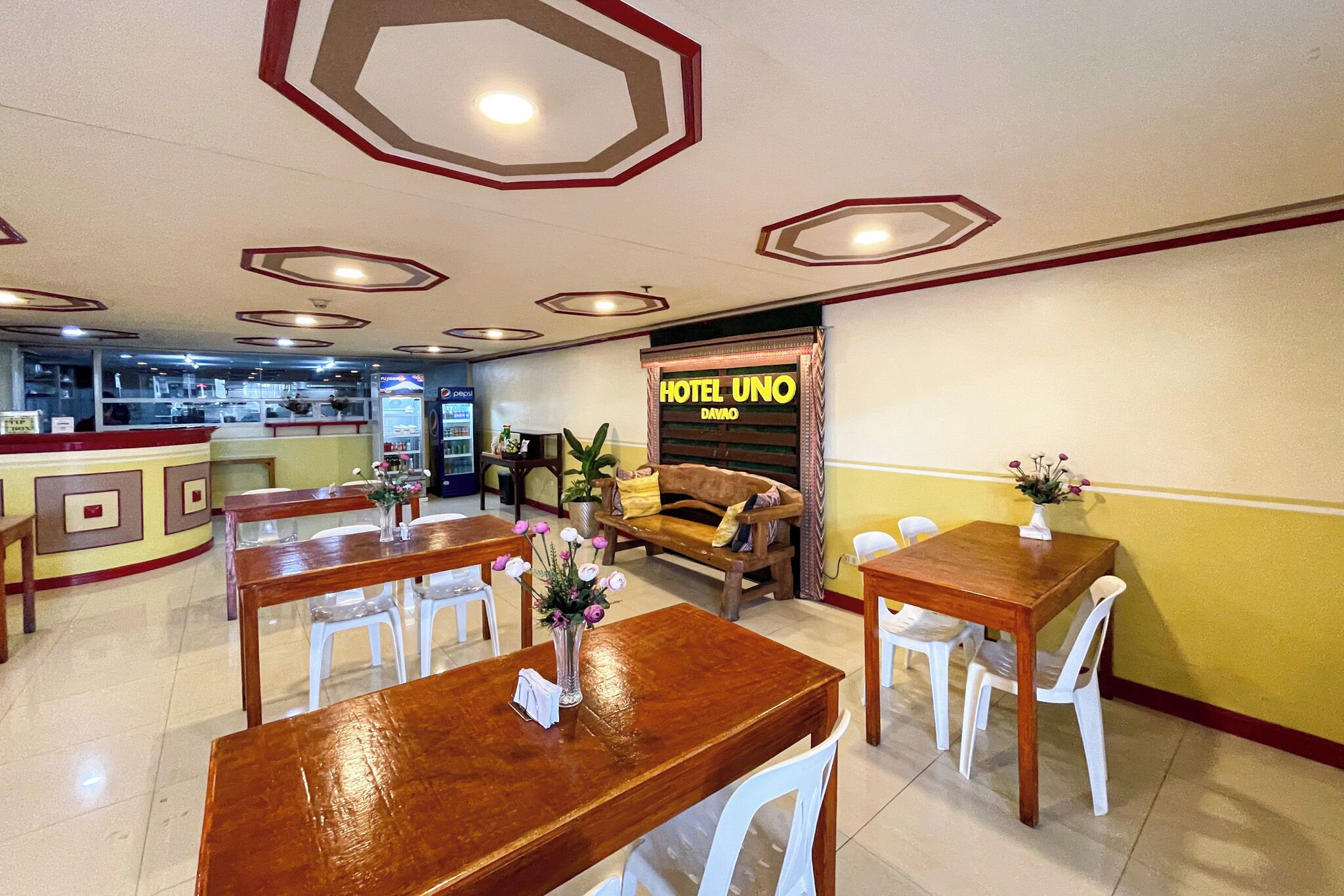 A hotel lobby with wooden tables and white chairs, a sofa, and a sign reading 'HOTEL UNO DAVAO'.