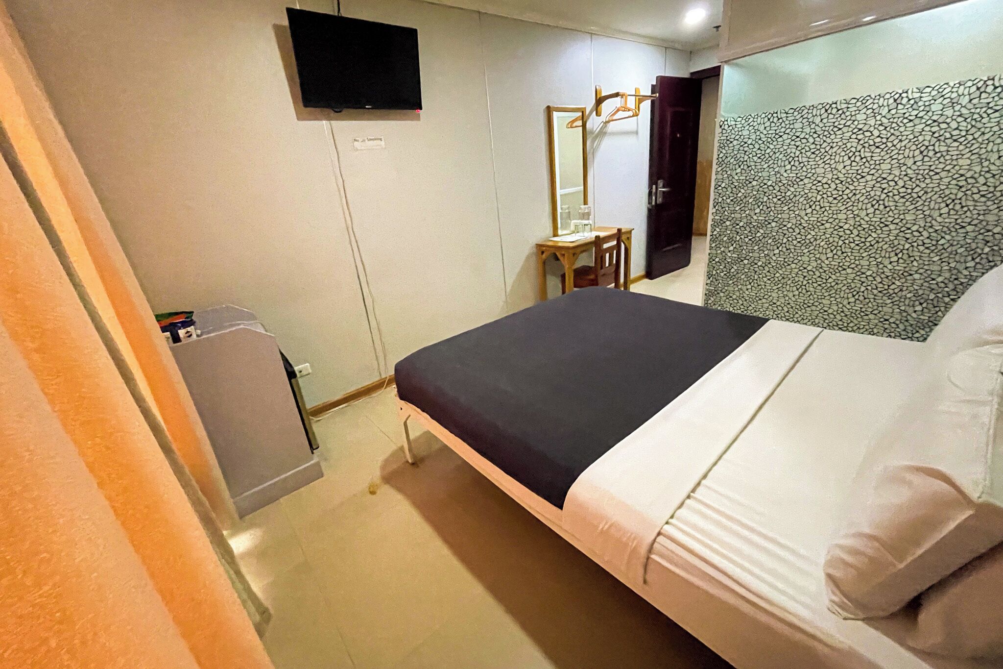 Une chambre d’hôtel avec un lit, un bureau, un miroir et une télévision.