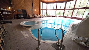 An indoor swimming pool with a hot tub, lounge chairs, and a view of the outdoors.