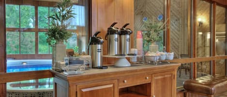 A buffet setup with a wooden counter, hot beverage dispensers, and a view of an outdoor pool.