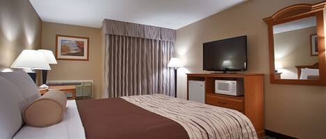 A hotel room with a bed, a television, a microwave, and a desk with a lamp.