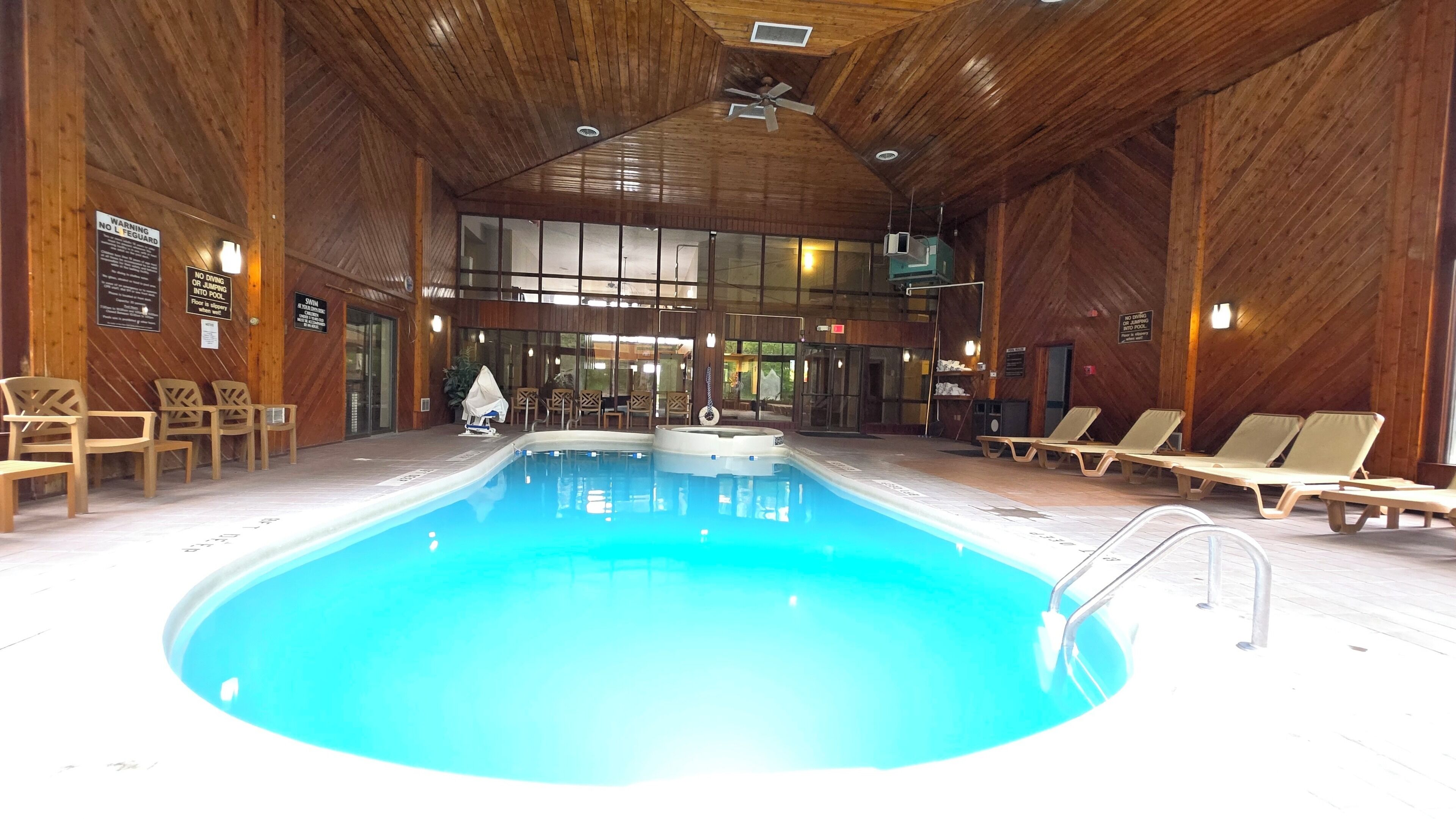 An indoor swimming pool with wooden walls, lounge chairs, and a sauna area.