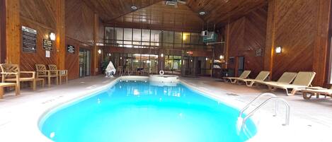 An indoor swimming pool with wooden walls, lounge chairs, and a sauna area.